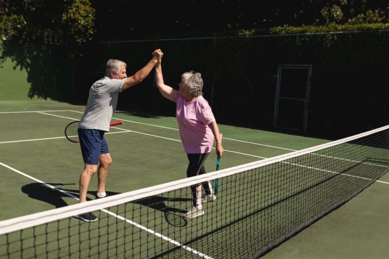 Older couple high-fiving on a tennis court