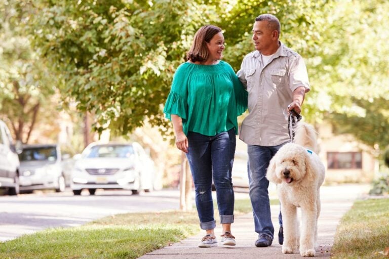 Older couple walking their dog on a neighborhood sidewalk